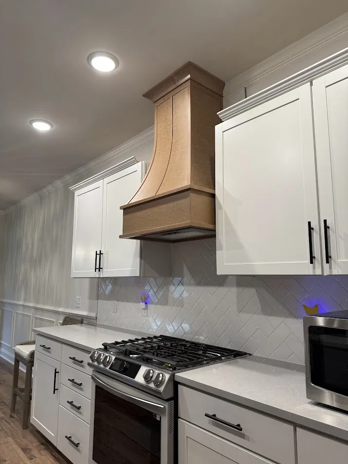 Kitchen with herringbone tile backsplash and custom wood range hood by CNB Renovations